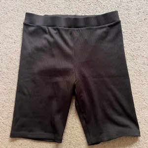 Svarta ribbade cykelshorts - Svarta cykelshorts med ribbad struktur och elastisk midja. De är knälånga och har en tight passform som sitter skönt på kroppen. Perfekta för träning eller en chill vardagslook. Aldrig använda 