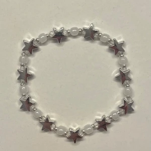 Pärlarmband med silvriga stjärnor - Hemgjort armband med vita pärlor och silvriga stjärnor. Stretchig modell som är lätt att ta på och av. Gjord med elastisk tråd och passar därför många storlekar! ❤️                                       Obs! -de små silverpärlorna kan tappa sin färg om de tvättas mycket i vatten.