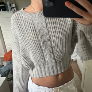 Beige/grå  stickad tröja NA-KD - Superfin beige/grå croppad stickad tröja från NA-KD med grov ribbstickning och en bred flätad detalj framtill. Tröjan har lång ärm och rund halsringning. Storlek xxs, i väldigt bra skick 