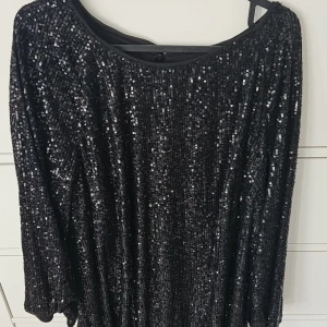 Svart paljettklänning från H&M - Glittrig svart klänning från H&M i storlek L, täckt med paljetter för maxad partykänsla. Modellen har trekvartsärm och rund halsringning, samt en snygg öppning i ryggen. Perfekt för dig som vill sticka ut och glänsa.