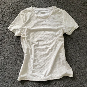 Vit spetsmönstrad t-shirt från JDY - Supersöt vit t-shirt från JDY i storlek XS med broderat spetsmönster och små hål för en luftig känsla. Klassisk rund hals och korta ärmar. Perfekt till sommaren!💕