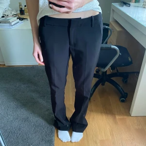 Svarta lågmidjade kostymbyxor från BikBok - Kostymbyxa i semi-stretchigt vävt material med medellåg midja, slim fit, raka ben som är lätt utsvängda nedtill och pressveck. Linning med hällor samt dold ögla, knapp och dragkedja framtill. Byxan har snedställda sidfickor fram och dekorativa stolpfickor bak.