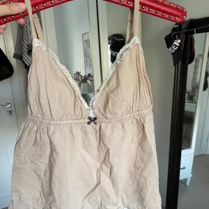 Beige linnetopp Odd Molly med spetsdetaljer - Supersöt beige linnetopp från Odd Molly med tunna justerbara axelband, spetskant vid v-ringningen och liten rosett framtill. 