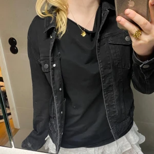 Svart jeansjacka från Vero Moda - Säljer en svart jeansjacka från Vero Moda i klassisk modell med knappar framtill och bröstfickor. Jackan har en snygg, lite tvättad look och är tillverkad i denim. Perfekt att slänga över en hoodie eller t-shirt för en chill vibe.
