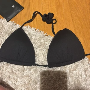 Svart trekantsbikini med knyt - En stilren svart trekantsbikini med knyt i nacken och ryggen. Klassisk modell med tunna band och mjukt, stretchigt material som formar sig snyggt. Perfekt för stranden eller poolen och enkel att matcha med olika underdelar.