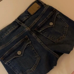 Mörkblå jeansshorts med rå kant - Snygga mörkblå jeansshorts från lager 157 med klassiska fickor bak och fram, rå kant nertill och detaljer i silver och koppar. Perfekta för varma dagar och enkel att matcha med allt. Tidlös modell med normal passform.