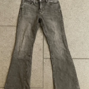 Grå bootcut jeans med låg midja - Snygga grå jeans med bootcut-modell och låg midja. Jeansen har klassisk femficksdesign och är tillverkade i ett mjukt denimtyg. Perfekta för dig som gillar en avslappnad men trendig look. Har inte använt byxorna mycket alls