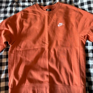 Orange sweatshirt från Nike - Säljer en snygg orange sweatshirt från Nike i storlek M. Tröjan har en klassisk rund halsringning och Nike-logga broderad i vitt på bröstet. Tillverkad i mjuk bomullsmix och har långa ärmar. Perfekt för en chill och sportig look.