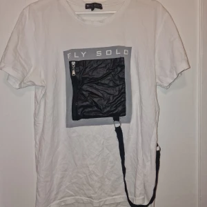 Vit t-shirt med svart ficka och tryck - Cool vit t-shirt från Ron Tomson LA. Fickan har en extra remdetalj som ger streetkänsla. Perfekt för dig som gillar unika detaljer och stilren design.