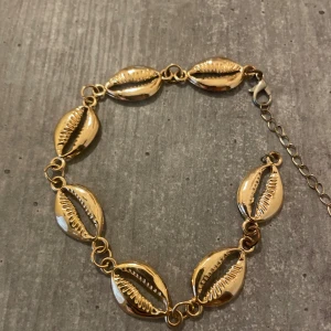 Guldigt armband med snäckskal - Snyggt armband i guldton med flera snäckformade länkar som ger en strandig och trendig vibe. Justerbar kedja med karbinlås gör att det passar de flesta handleder. Perfekt accessoar för att lyfta din outfit med en cool detalj.