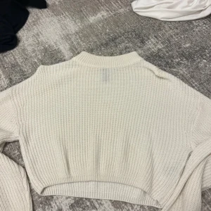 Vit croppad stickad tröja H&M Divided - Säljer en vit croppad stickad tröja från H&M Divided i storlek XS. Tröjan har en ribbad, högre halsringning och är gjord i ett grovstickat material. Perfekt för lager-på-lager och chill vibes.
