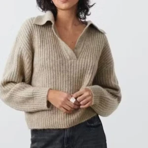 Beige stickad tröja Gina Tricot XS - Supermysig beige stickad tröja från Gina Tricot i storlek XS. Tröjan har en bred krage, v-ringning och ribbad struktur. Perfekt för lager-på-lager och chill dagar. Långärmad och loose fit för en avslappnad vibe.