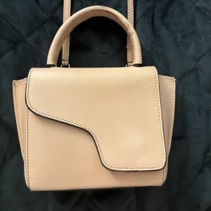 ATP väska  - Snygg beige handväska i skinn med unik asymmetrisk lockdesign. Väskan har både handtag och avtagbar axelrem med silvriga metalldetaljer. Perfekt storlek för det viktigaste och stilren look som passar till många outfits. Defekter finns men jag själv tänker inte på det så mycket när man har på sig den💓 Pris kan diskuteras💕
