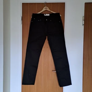 Svarta jeans från Dressmann - Svarta jeans från Dressmann med klassisk femficksdesign och raka ben. Byxorna har normal passform och är tillverkade i ett slitstarkt bomullstyg med lite stretch. Perfekta för dig som gillar en enkel och stilren look.