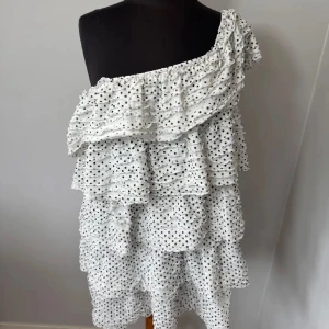 Vit prickig volangklänning offshoulder - Supersöt kort volangklänning i vitt med svarta prickar. Offshoulder-modell med flera lager volanger som ger en fluffig och lekfull look. Perfekt för sommarens alla tillfällen. Lätt och luftig, passar dig som gillar en trendig och avslappnad stil. Den är i storlek L men sitter som på bilderna på mig som vanligtvis brukar ha S🩷