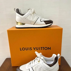 Louis Vuitton Run Away Trainer sneakers - Storlek 36/37Exklusiva Louis Vuitton Run Away Trainer sneakers i vitt och brunt med klassiskt monogrammönster. Skorna har gulddetaljer vid hälen, LV-logga på sidan och snörning. Tillverkade i en mix av skinn och textil för en lyxig känsla. Perfekta för dig som vill sticka ut.