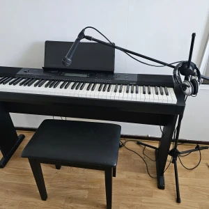 Digital piano Casio,mikrofon,stol och mikrofon hållare - Bilderna visar ett digitalpiano av märket Casio, modell CDP-220R, med tillhörande notställ, mikrofon, hörlurar och bänk. Perfekt för dig som vill skapa musik hemma eller öva på att spela piano och sjunga samtidigt. Utrustningen ser modern ut och passar både nybörjare och mer erfarna musiker.