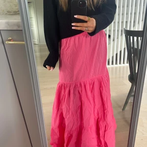 Rosa volangkjol i lång modell - Säljer en långkjol i stark rosa färg med volanger och avslappnad passform. Kjolen har en luftig och flowy känsla, perfekt för dig som gillar färg och vill sticka ut. Materialet känns lätt och passar bra till sneakers eller sandaler.