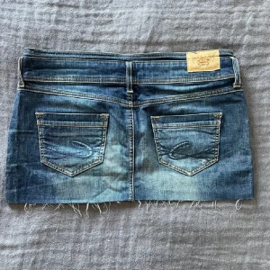 Lågmidjad jeanskjol - Snygg lågmidjad jeanskjol med coola detaljer. Sitter jätte skönt och har en fin färg. Storlek 38 och passar mig som vanligtvis har M/38. Materialet är hyfsat stretchigt.