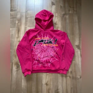 Spi5er hoodie y2k usa - Säljer en cool rosa hoodie med en unik spindelnätsdesign och textdetaljer på framsidan. Hoodien har en stor stjärna på baksidan och färgglada stjärnor på ärmarna. Perfekt för en avslappnad stil.