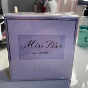 Miss Dior Eau de Parfum - Säljer en elegant och tidlös Miss Dior Eau de Parfum från Dior. Den kommer i en stilren förpackning med en ljusrosa ton och silverdetaljer. Perfekt för den som älskar en klassisk och feminin doft.