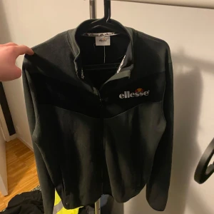 Svart jacka från Ellesse - Säljer en svart jacka från Ellesse med dragkedja och långärmade ärmar. Jackan har en stilren design med Ellesse-loggan på bröstet. Perfekt för en casual look.