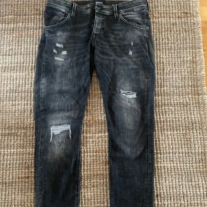 Svarta jeans med slitningar - Snygga svarta jeans med snygga slitningar och en slim fit passform. Jeansen är i storlek 33/30. Modellen är Glenn och är en slim modell. Jeansen är i väldigt bra skick och knappt använts. Hör av dig vid funderingar. // Olle