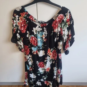 Blommig klänning från KappAhl - Snygg blommig klänning med korta ärmar och elastisk halsringning. Klänningen har ett färgglatt blommönster i rött, blått och grönt på en svart bakgrund. Perfekt för en somrig look!