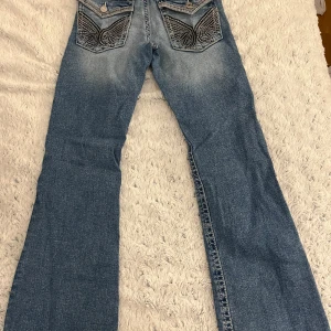Blå jeans med broderade fickor från Gina Tricot - Snygga blå jeans från Gina Tricot med unika broderade detaljer på bakfickorna. Jeansen har en bootcut-stil och är perfekta för en avslappnad look. De har en klassisk femficksdesign och en bekväm passform.