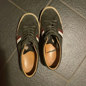 Svarta sneakers från Moncler - Snygga svarta sneakers från Moncler med vita och vinröda detaljer. Skorna har snörning och en klassisk design med en bekväm innersula. Perfekta för en stilren look. Endast skor tillkommer