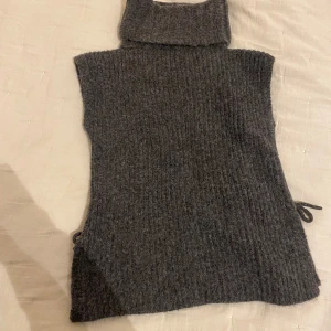 Polokragge stickade ärmlös  - Säljer en mysig grå stickad väst med polokrage. Västen har en ribbad design och knytning i sidorna . Perfekt för lager-på-lager under kyliga dagar. Storleken är M. 