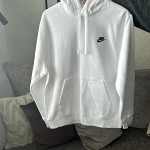 Vit hoodie från Nike - Säljer en stilren vit hoodie från Nike med klassisk logga på bröstet. Tröjan har en känguruficka och justerbar huva med dragsko. Perfekt för en avslappnad stil. Storlek M. Inga fläckar. 