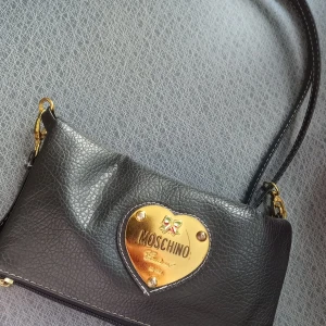 Svart axelväska från Moschino - Säljer denna svarta axelväskan från Moschino med ett hjärtformat guldfärgat. Axelbanden är avtagbara 🖤▪️