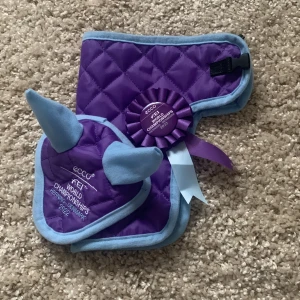 Lila och blå käpphästhuva, täcke och rosett - Snygg lila och blå käpphästhuva, täcke och rosett, perfekt för tävlingar. Broderad text med 'FEI World Championships 2022'. Quiltad design med mjukt material!