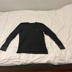 Mörkgrå långärmad tröja från Polo Ralph Lauren - Säljer en stilren mörkgrå långärmad tröja från Polo Ralph Lauren. Tröjan har en liten broderad logotyp på bröstet och är tillverkad i ett mjukt material. Perfekt för en avslappnad och snygg look.