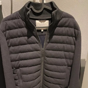 Svart quiltad jacka från Woolrich - Snygg svart quiltad jacka från Woolrich med dragkedja framtill. Jackan har en ribbad krage. Perfekt för våren. Jag har alla lappar kvar till den. Använd 2 gånger. 