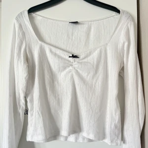 Vit långärmad topp från Gina Tricot - Säljer en söt vit långärmad topp från Gina Tricot. Toppen har ett diskret mönster och en liten svart rosett framtill