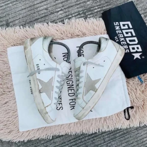 Vita sneakers från Golden Goose - Snygga vita sneakers från Golden Goose med den ikoniska stjärndetaljen i grått på sidan. Skorna har en vintage-look med smutsiga detaljer och snörning framtill. Perfekta för en avslappnad stil.