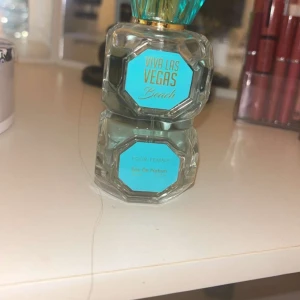 Viva Las Vegas Beach Eau de Parfum - Säljer en elegant Viva Las Vegas Beach Eau de Parfum. Flaskan är åttakantig och genomskinlig med turkosa detaljer och en gyllene hals. Perfekt för den som älskar fräscha och somriga dofter.