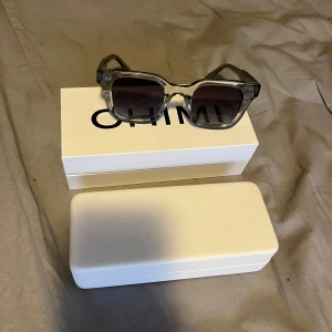 Chimi 04 grey - Snygga transparenta solglasögon från Chimi fyrkantig form och mörka linser. Perfekta för en stilren look. Allt medkommer i köpet! De är använda ca 5-6 gånger men skicket är som gott som ny. Om du har några frågor så tveka inte att höra av dig. MVH Luxtrend
