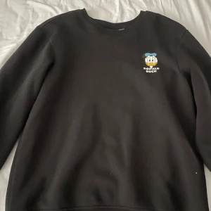 Svart tröja med Kalle Anka-motiv - Säljer en svart tröja med Kalle Anka-tryck på bröstet och stort motiv på baksidan med texten 'Walt Disney's Comics'. Perfekt för Disney-fans! 🖤