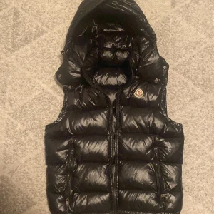 Moncler väst - Säljer en snygg svart dunväst från Moncler med huva och dragkedja. Västen har två fickor med dragkedjor och Moncler-logga på bröstet. Perfekt för kyliga dagar! Och perfekt till en stilig outfit priset kan diskuteras passar båda xs och s