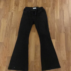 Svarta byxor från Lindex - Snygga svarta byxor från Lindex med en bootcut-stil. Perfekta för en trendig look. Byxorna har en klassisk design med knapp och dragkedja framtill.
