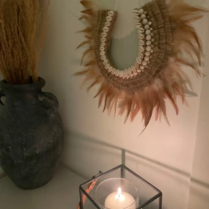 Dekorativt halsband med snäckor och fjädrar - Unikt dekorativt halsband med vita snäckor och bruna fjädrar. Perfekt som väggdekoration för att ge en bohemisk känsla till ditt hem. Halsbandet har en naturlig och jordnära stil med en kombination av texturer.