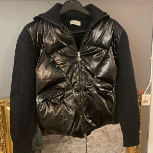 Svart Moncler Cardigan - Snygg svart cardigan från Moncler med glansig finish och stickade ärmar. Jackan har en dragkedja framtill och en klassisk Moncler-logga på ärmen. Perfekt för att hålla stilen i kyligare väder. Storlek S samt mycket sparsamt använd. Pris kan diskuteras!