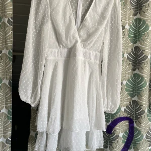 Vit prickig klänning - Säljer en söt vit klänning med prickigt mönster och v-ringad design. Klänningen har långa ärmar och en flerdelad kjol som ger en fin volangeffekt. Perfekt för sommarens alla tillfällen!