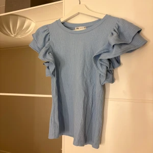 Volang topp från Zara - Säljer en ljusblå ribbad topp från Zara med volangdetaljer på ärmarna. Hör av er vid funderingar eller om ni vill ha bilder med hur plagget sitter på mig. Titta gärna in mina andra plagg!