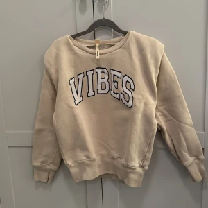 Beige sweatshirt från Betterose - Säljer en beige sweatshirt från Betterose med texten 'VIBES' i blått på framsidan. Tröjan har långa ärmar och en avslappnad passform. Om man kollar på sista bilden ser man att armarna är lite stora. Den här tröjan har jag köpt på Lucca