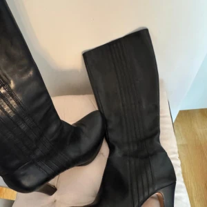 Svarta stövlar med klack - Eleganta svarta stövlar i skinn med klack och dekorativa sömmar längs skaftet. Perfekta för en stilren look. Används typ två gånger