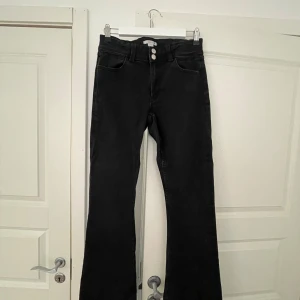 Svarta bootcut jeans från Gina Tricot - Säljer ett par svarta bootcut jeans från Gina young tall med låg midja och två silverfärgade knappar. Jeansen har klassisk femficksdesign och är i stretchigt denimtyg. Perfekta för dig som gillar en tidlös look med lite utsvängda ben. Nästan aldrig använda, pris går att diskutera och skriv för fler bilder!